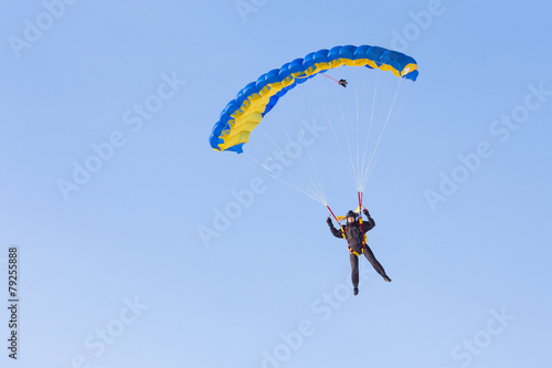 Skydiver on blue and yellow parachute on background blue sky