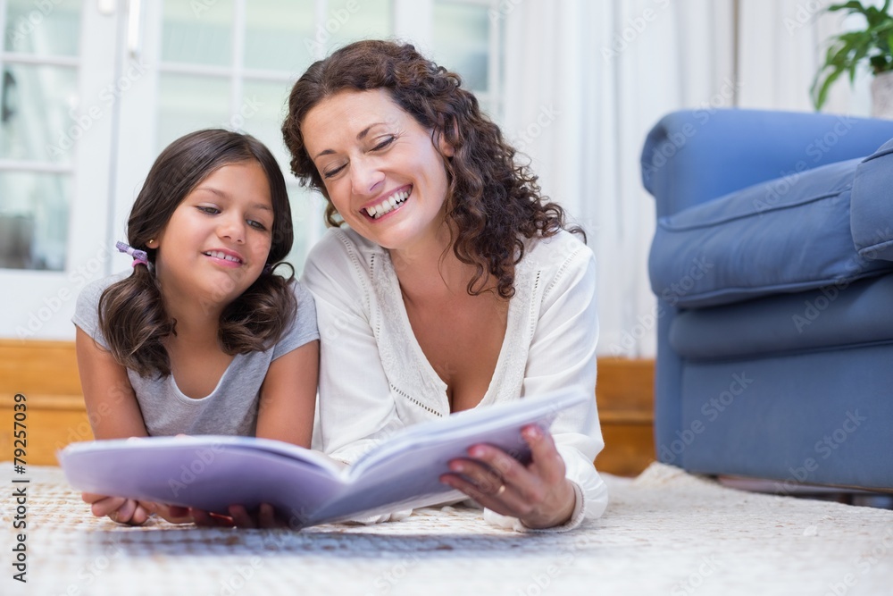 Happy mother and daughter lying on the floor and reading a book Happy mother and daughter lying on the floor and reading a book