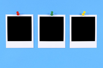 Row or line of three blank polaroid style photo frame prints pinned to blue background