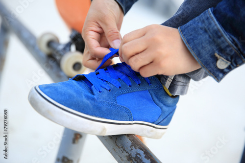 skateboarder hands tying shoelace on skatepark
