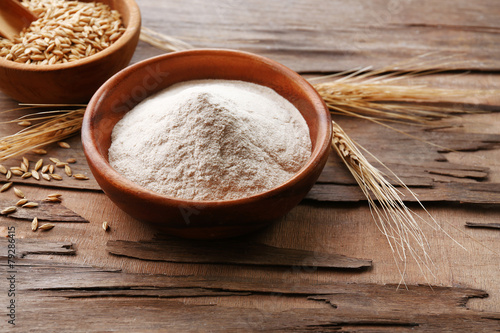 Flour and grains in bowls with ears on wooden background