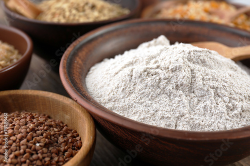 Flour and different grains in bowls on wooden table