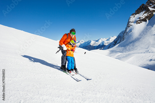Dad teach little son to ski in mountains