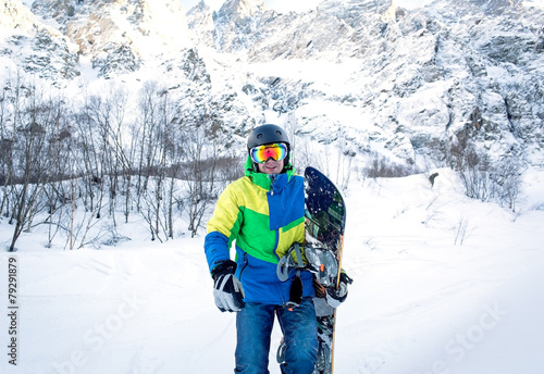 The man with the snowboard is on the background of mountains