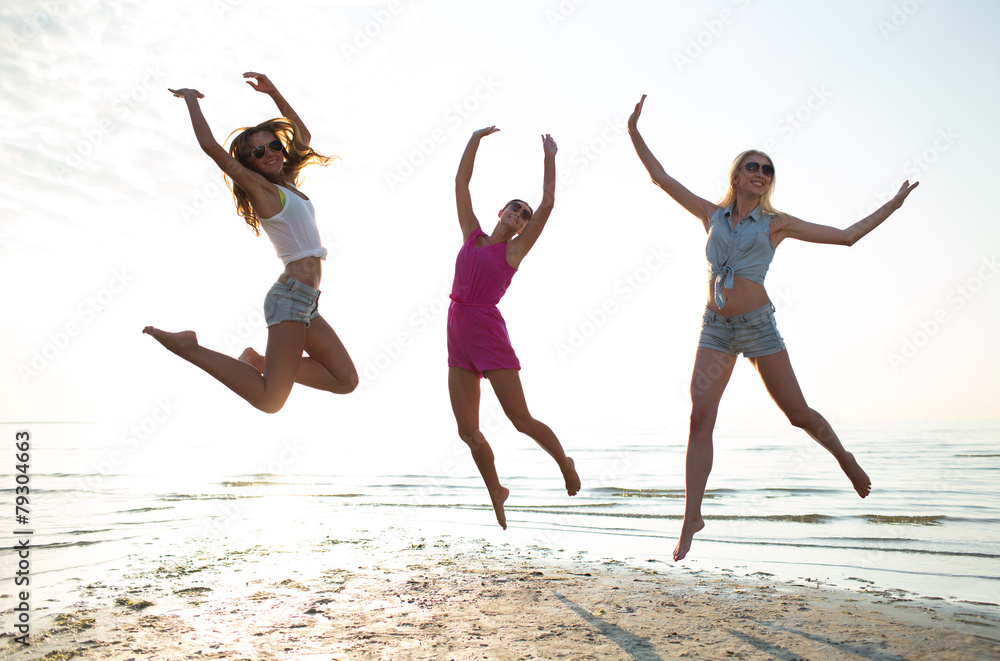 happy female friends dancing and jumping on beach