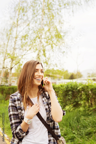 Happy teenage girl in park speaking on smartphone