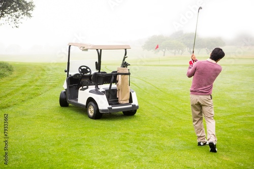 Golfer teeing off next to his golf buggy