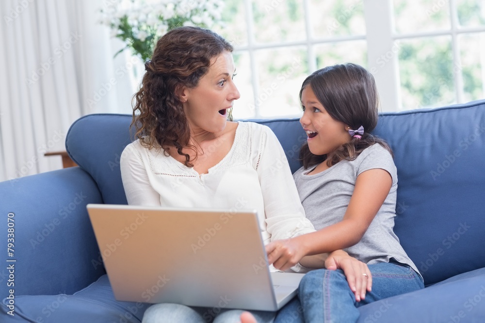 Happy mother and daughter sitting on the couch and using laptop Happy mother and daughter sitting on the couch and using laptop