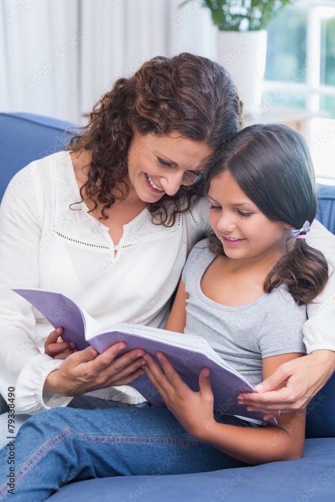 Happy mother and daughter sitting on the couch and reading book Happy mother and daughter sitting on the couch and reading book