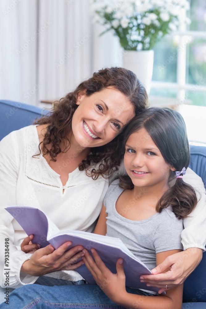 Happy mother and daughter sitting on the couch and reading book Happy mother and daughter sitting on the couch and reading book