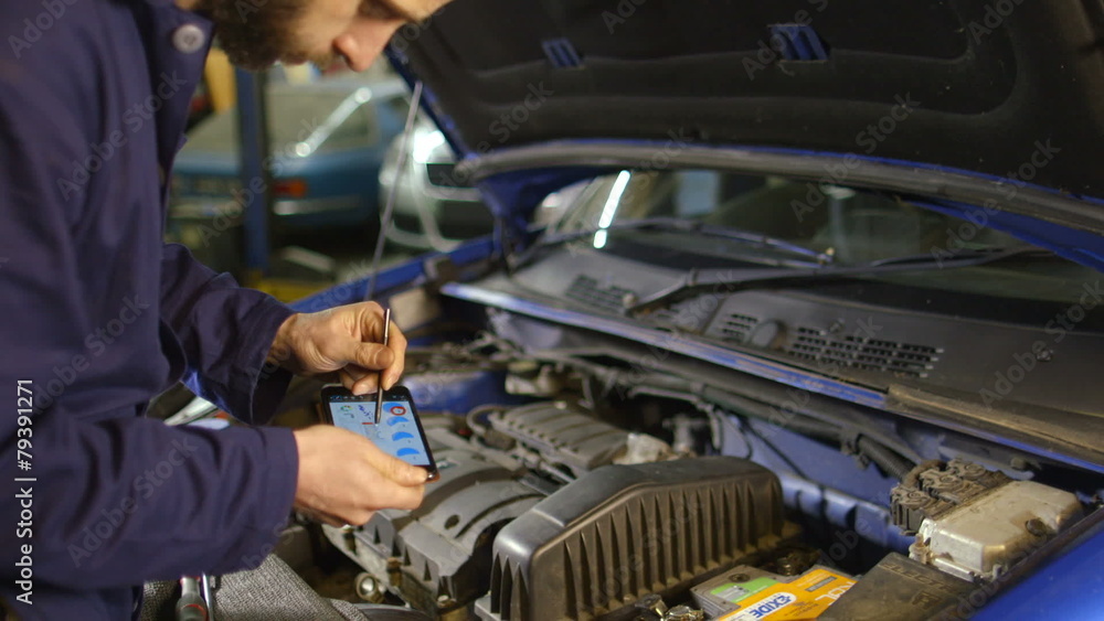 Mechanic entering data into a diagnostic tool while doing routine maintenance on a car Mechanic entering data into a diagnostic tool while doing routine maintenance on a car