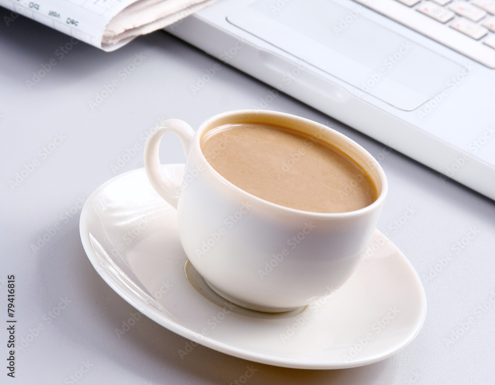 Cup of coffee near the laptop and newspapers Cup of coffee near the laptop and newspapers