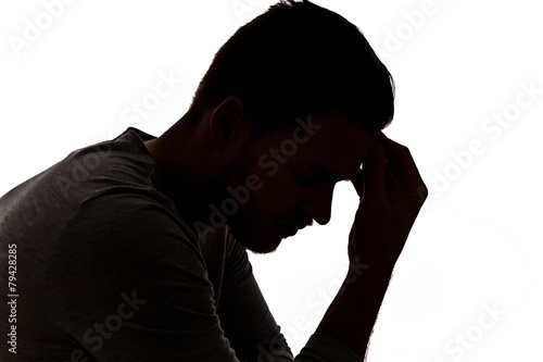 Desperate young man in silhouette holding his head photo