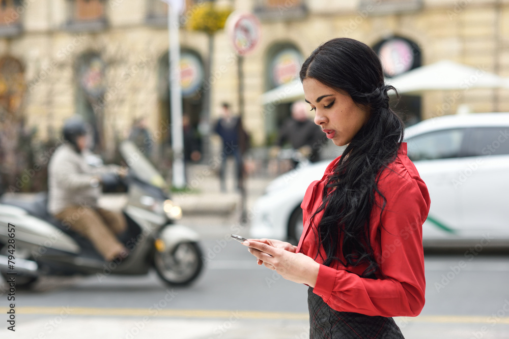 Fototapeta premium Hispanic stewardess in urban background looking at her mobile ph