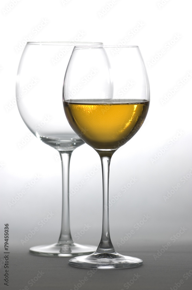 Two tall glasses, empty and filled with white wine Two tall glasses, empty and filled with white wine
