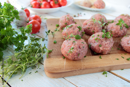 Raw meat balls with herbs on wooden board