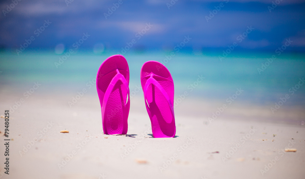 Naklejka premium Pink vibrant beach flip flops on white sand on sea background