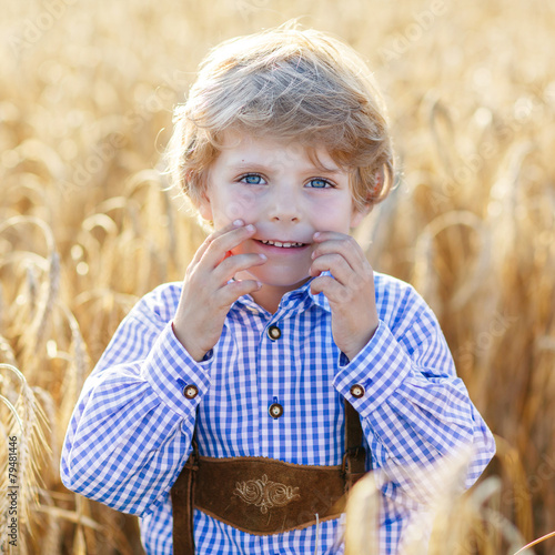 Funny little kid boy in leather shors, walking  through wheat fi photo