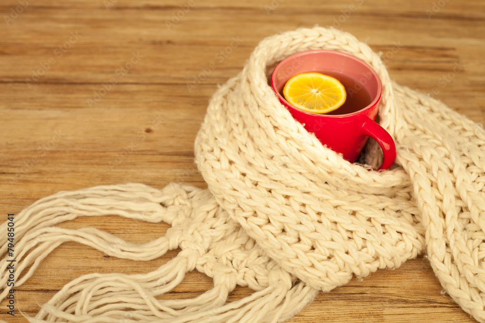 Sickness concept: Cup of hot tea and lemon wrapped with a scarf