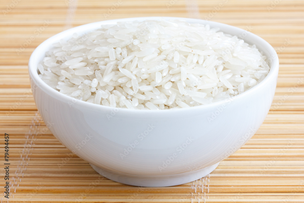 Bowl of uncooked white long grain rice on a bamboo mat. Bowl of uncooked white long grain rice on a bamboo mat.
