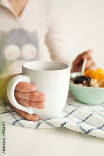 Woman holds tea cup and spoon with porridge and fruits