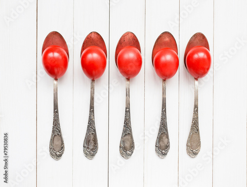 Red Easter eggs in old spoons on white wooden background
