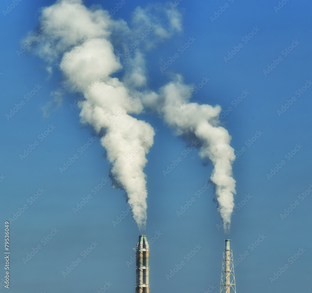 Blurred - Plant stack with white smoke against blue sky Blurred - Plant stack with white smoke against blue sky