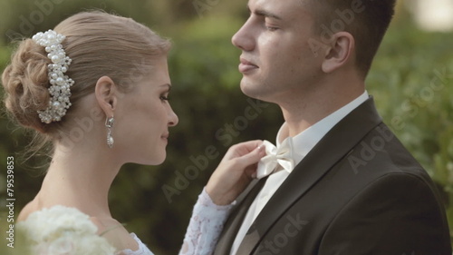 Happy bride straightens bow of groom standing among the leaves