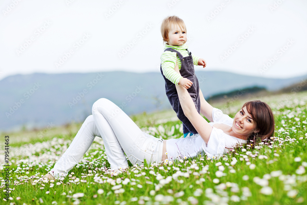 Fototapeta premium Happy mother are playing with baby in flowers field