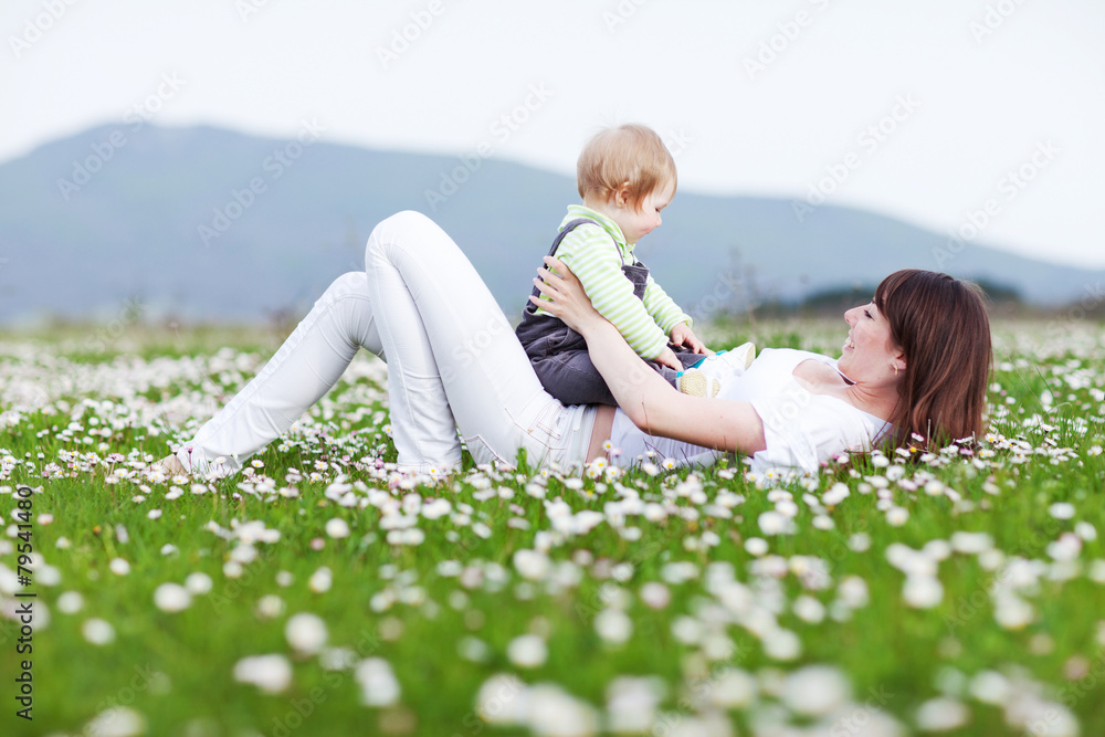 Fototapeta premium Happy mother are playing with baby in flowers field