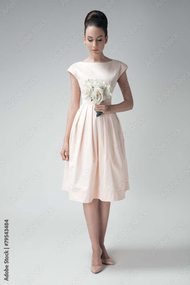 Beautiful woman in pink retro dress. White roses in hand. Gray b Beautiful woman in pink retro dress. White roses in hand. Gray b