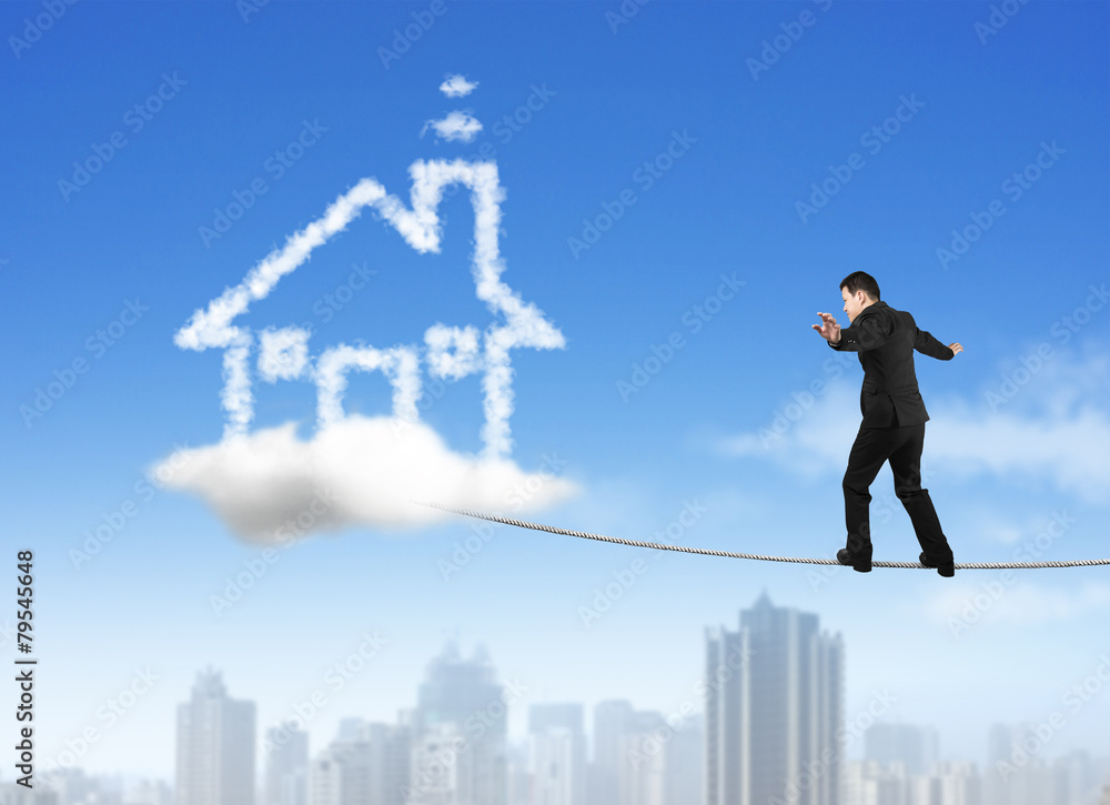 Businessman walking on rope toward house shape cloud with skyscr Businessman walking on rope toward house shape cloud with skyscr