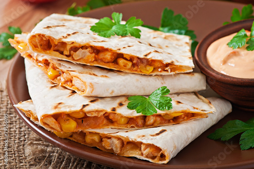 Mexican Quesadilla sliced with vegetables and sauces on the tabl
