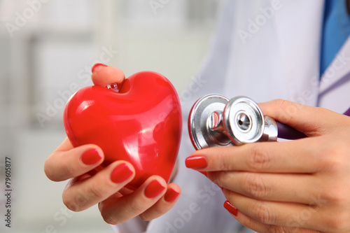 Doctor with stethoscope examining red heart, isolated on white