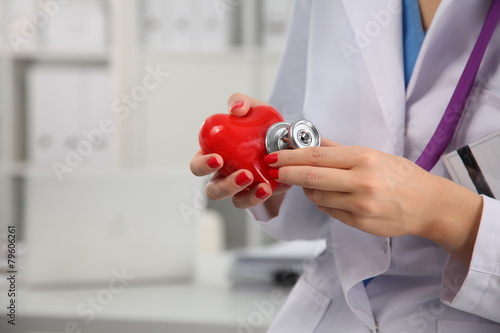 Female doctor with stethoscope holding heart over white