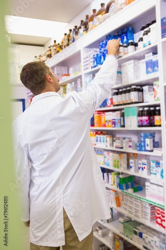 Pharmacist in lab coat taking jar from shelf