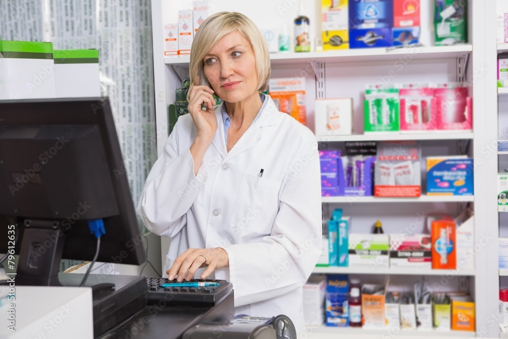Blonde pharmacist using computer while phoning