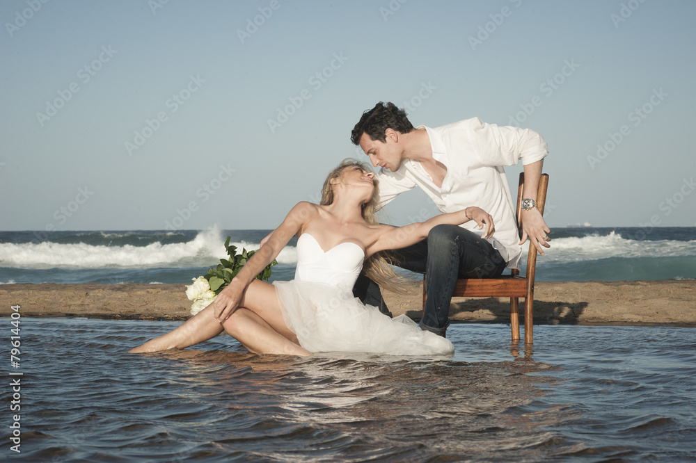 Young beautiful couple sitting at water's edge flirting in love