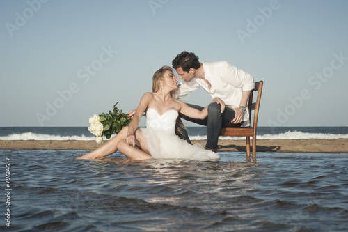 Young beautiful couple sitting at water's edge flirting in love