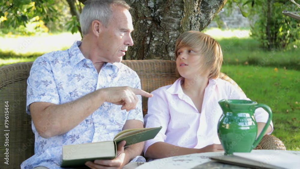 MS, Father and son sitting on bench in garden reading and talking MS, Father and son sitting on bench in garden reading and talking