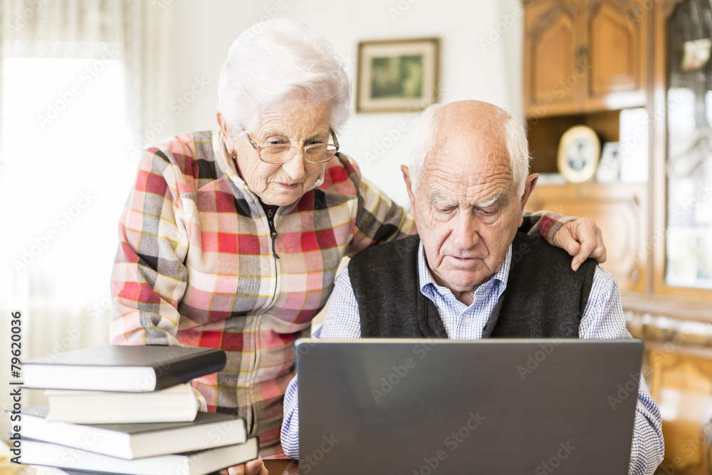 Senior couple looking for information in books and internet Senior couple looking for information in books and internet