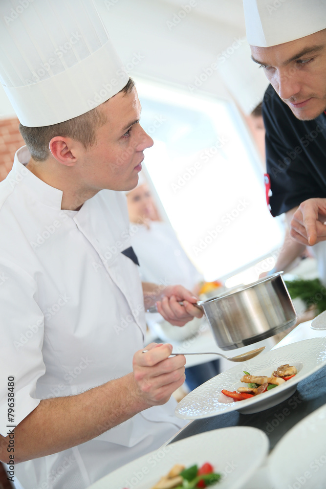 Chef with young cook in kitchen preparing dish Chef with young cook in kitchen preparing dish