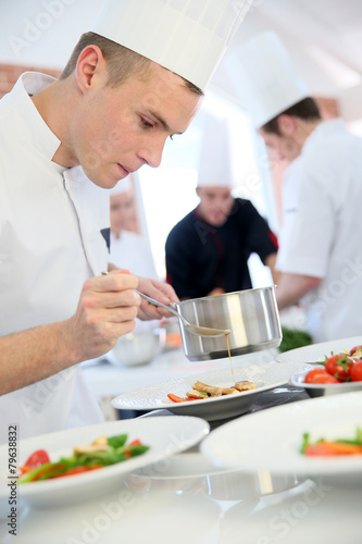 Young cook pouring sauce on dish
