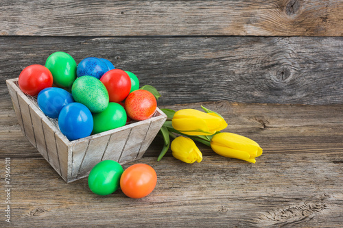 Easter eggs in basket and yellow tulips on wooden background
