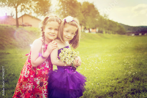 Two cute blonde little girls in dresses with flowers in spring