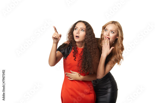Two surprised girls friends with opened mouths pointing to blank