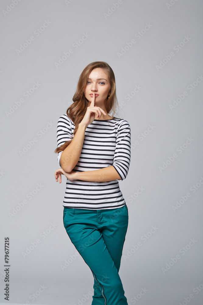 Young woman with finger on lips, on gray background Young woman with finger on lips, on gray background