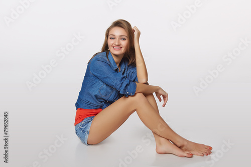 Denim style portrait of teen girl on the floor, over gray backgr