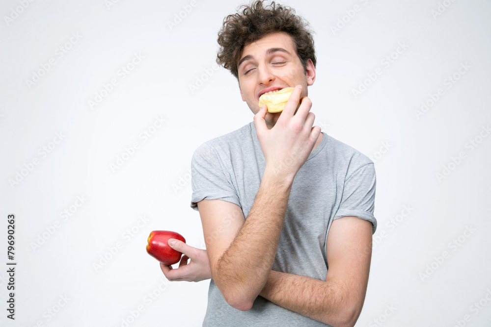 Young man holding apple and eating unhealthy donut Young man holding apple and eating unhealthy donut