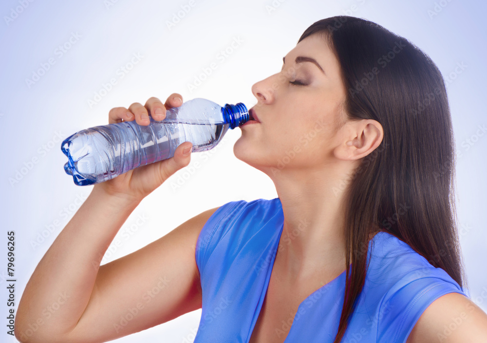 Woman drinking water from bottle on a blue background Woman drinking water from bottle on a blue background
